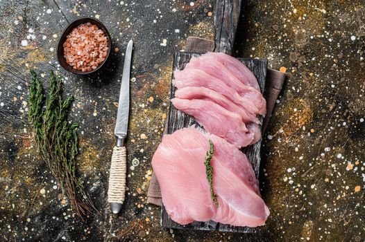 Sliced Raw turkey breast fillet meat on a cutting board with butcher knife. Brown background. Top View.