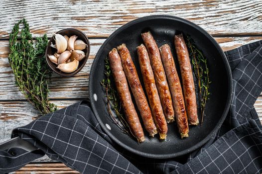 Fried beef and pork meat sausage in a pan with italian herbs and cheese. White wooden background. Top view.