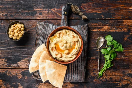 Hummus paste with pita bread, chickpea and parsley in a wooden bowl. Dark wooden background. Top view.