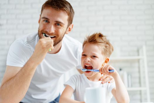 Dad and little son brushing teeth together in bathroom