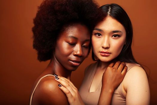 young pretty asian, afro woman posing cheerful together on brown background, lifestyle diverse nationality people concept close up
