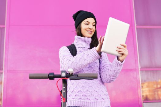 Woman in her twenties with electric scooter using digital tablet outdoors. Lifestyle concept.