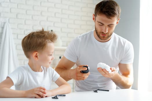 Father teaches his little son how to shave face in bathroom