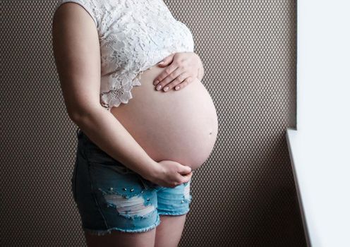 The hands of a pregnant girl hold their stomach, waiting for the birth of a child.