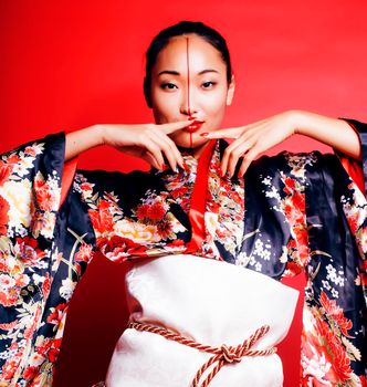 young pretty geisha on red background posing in kimono, oriental