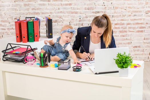 Businesswoman mother woman with a daughter working at the laptop. At the workplace, together with a small child