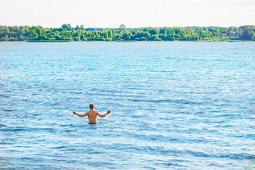 A man with a bare body has put his hands to the sides and is going to dive into the water of the lake in the open air, nature background.