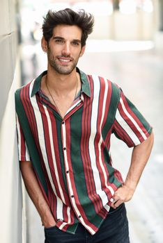 Handsome young man with dark hair and modern hairstyle wearing casual clothes in urban background.