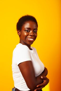 pretty young african american woman with curly hair posing cheerful gesturing on yellow background, lifestyle people concept close up