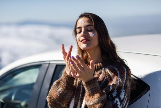 Young woman applying sunscreen on her face in snowy mountains in winter, in Sierra Nevada, Granada, Spain. Female wearing winter clothes.