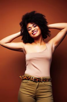 pretty young african american woman with curly hair posing cheerful gesturing on brown background, lifestyle people concept closeup