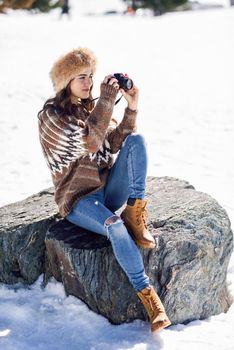 Young woman taking photographs in the snowy mountains in winter, in Sierra Nevada, Granada, Spain. Female wearing winter clothes.