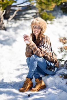 Female wearing winter clothes drinking hot coffee. Young woman enjoying the snowy mountains in winter, in Sierra Nevada, Granada, Spain.