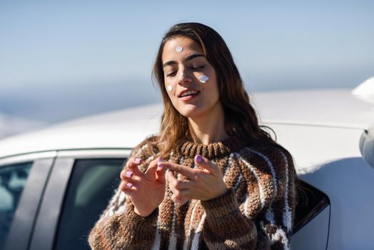 Young woman applying sunscreen on her face in snowy mountains in winter, in Sierra Nevada, Granada, Spain. Female wearing winter clothes.