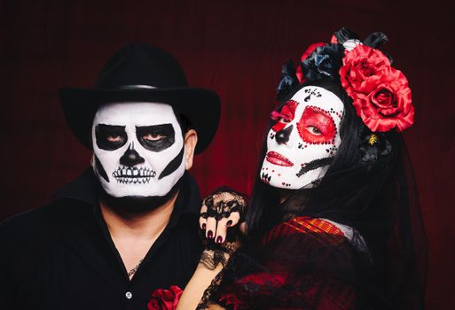 beautiful woman with a sugar skull makeup with a wreath of flowers on her head and a skeleton man in a black hat