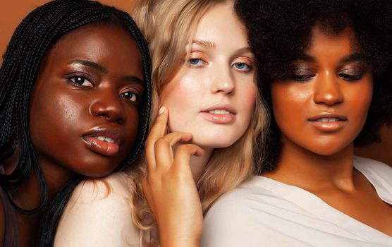 young pretty african and caucasian women posing cheerful together on brown background, lifestyle diverse nationality people concept close up