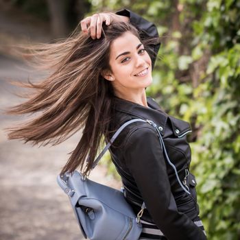 Young woman moving her hair in urban background wearing leather jacket