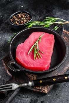 Fresh Raw tuna steak with rosemary in a pan. Black background. Top view.