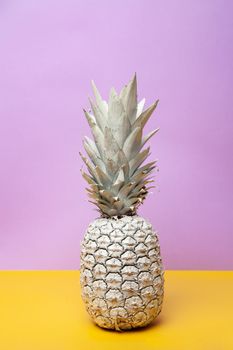 White whole ripe pineapple on yellow table on violet background in contemporary studio