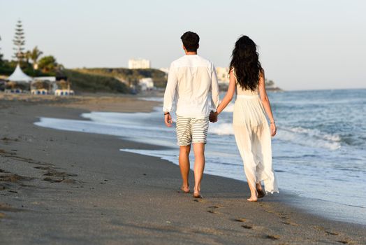 Young happy couple walking in a beautiful beach. Funny Man and woman wearing casual clothes. Rear view.