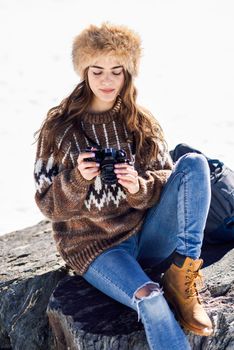 Young woman taking photographs in the snowy mountains in winter, in Sierra Nevada, Granada, Spain. Female wearing winter clothes.