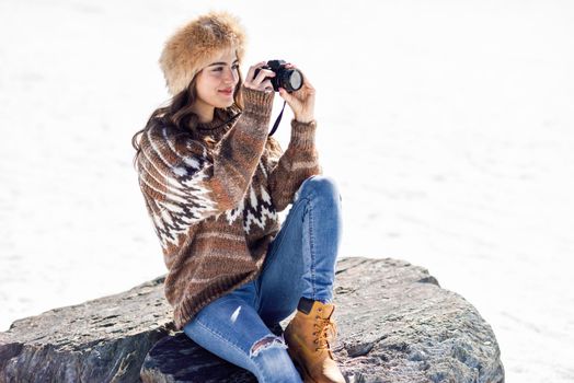 Young woman taking photographs in the snowy mountains in winter, in Sierra Nevada, Granada, Spain. Female wearing winter clothes.