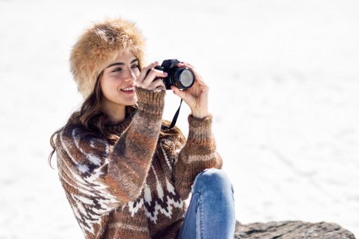 Young woman taking photographs in the snowy mountains in winter, in Sierra Nevada, Granada, Spain. Female wearing winter clothes.