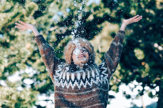 Young woman enjoying the snowy mountains in winter, in Sierra Nevada, Granada, Spain. Female wearing winter clothes playing with snow.