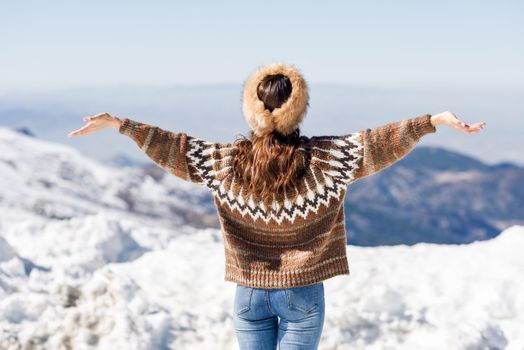 Rear view of woman enjoying the snowy mountains in winter, in Sierra Nevada, Granada, Spain. Female wearing winter clothes opening her arms.