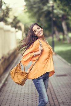 Young woman with moving hair wearing casual clothes and modern bag in urban background. Happy girl with wavy hairstyle in the wind.