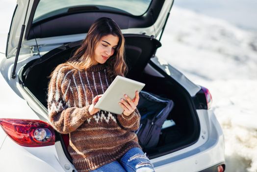 Young traveler woman using digital computer in snowy mountains in winter, in Sierra Nevada, Granada, Spain. Female wearing winter clothes.