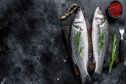 Raw seabass fish on a cutting board with spices, herbs. Black background. Top view. Copy space.