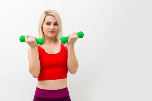 Athletic woman pumping up muscles with dumbbells on gray background