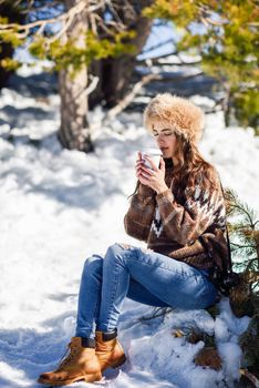 Female wearing winter clothes drinking hot coffee. Young woman enjoying the snowy mountains in winter, in Sierra Nevada, Granada, Spain.