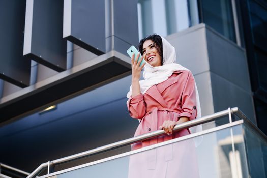 Young Muslim Woman wearing hijab headscarf recording voice note with a smartphone in a office building. Business background.