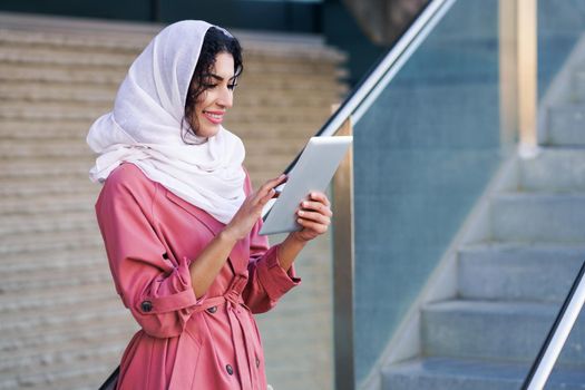 Young Arab woman wearing hijab headscarf using digital tablet in business environment.