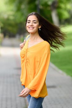 Young woman with moving hair wearing casual clothes in urban background. Happy girl with wavy hairstyle in the wind.