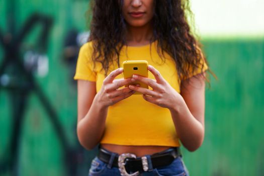 Young Arab woman texting a text message with her smartphone against green urban wall.