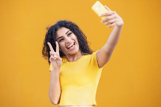 Funny Arab woman taking selfie photograph with smartphone. Curly hair female.