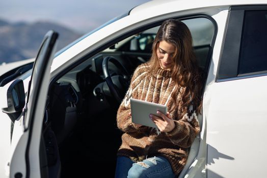 Young traveler woman using digital computer in snowy mountains in winter, in Sierra Nevada, Granada, Spain. Female wearing winter clothes.