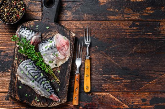 Cut smoked mackerel fish with herbs. Dark wooden background. Top view. Copy space.