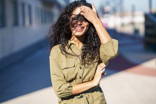 Young Arab Woman with curly hair in her face on urban yellow wall