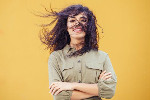 Young Arab Woman with curly hair in her face on urban yellow wall