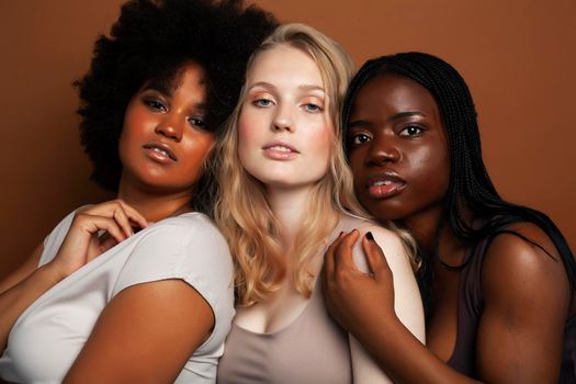 young pretty african and caucasian women posing cheerful together on brown background, lifestyle diverse nationality people concept close up