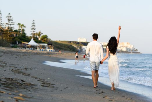 Young happy couple walking in a beautiful beach. Funny Man and woman wearing casual clothes. Rear view.