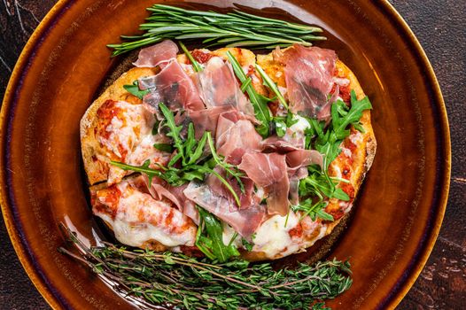Pizza with prosciutto parma ham, arugula salad and parmesan cheese in a rustic plate. wooden background. Top view.