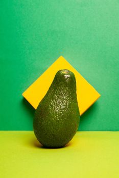 Fresh ripe green avocado with textured shell placed on table against bright yellow and green background