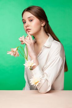 Crop female model with fresh flowers growing from blouse sleeves touching face against green background
