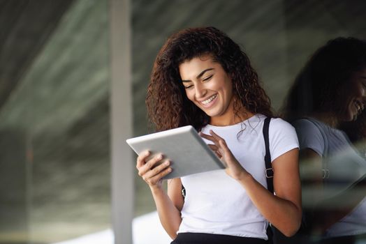 Happy young Arab woman using digital tablet in business background. Happy girl wearing sportswear with toothy smile.