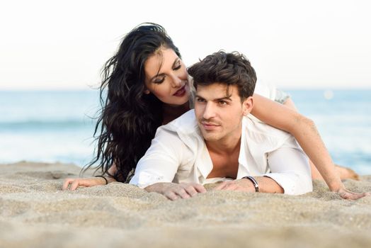 Young happy couple lying on the sand in a beautiful beach. Funny Man and woman wearing casual clothes.